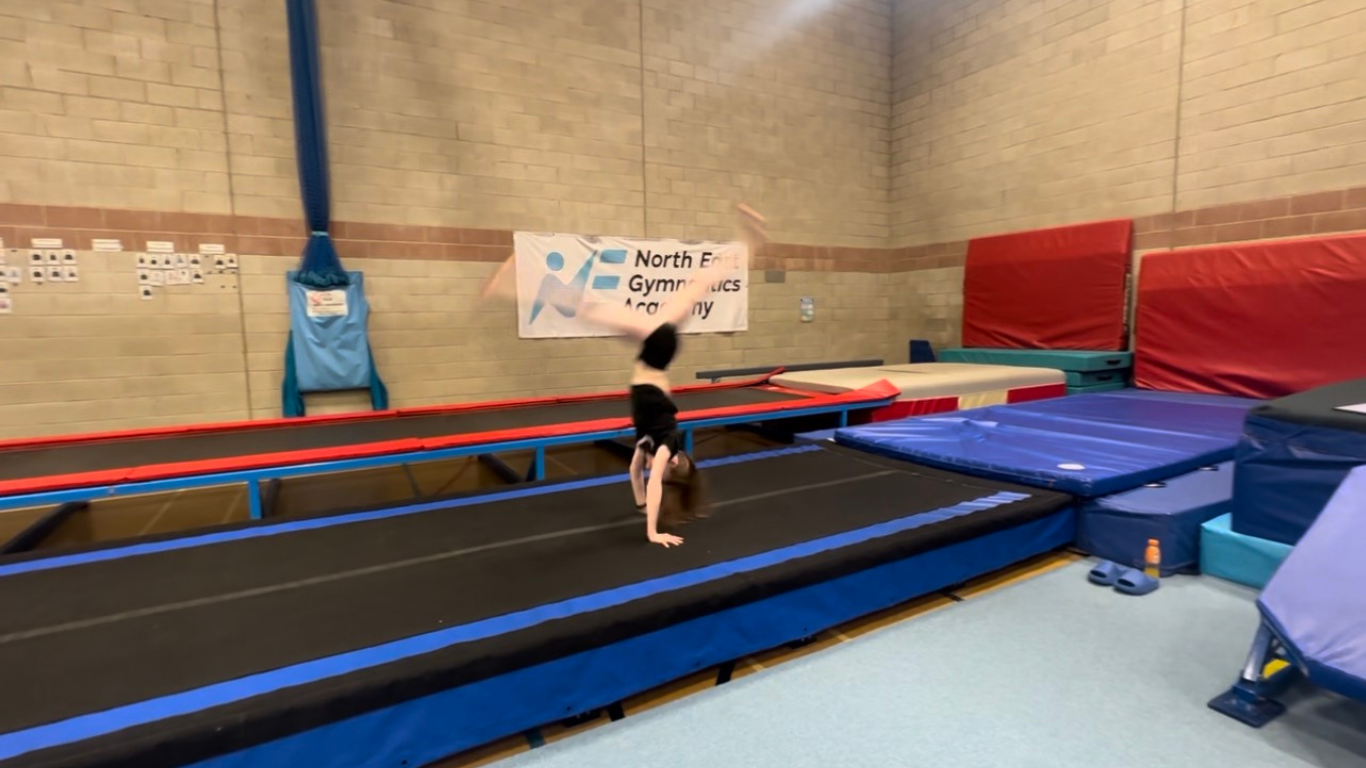 A gymnast in a split handstand position on the tumble track
